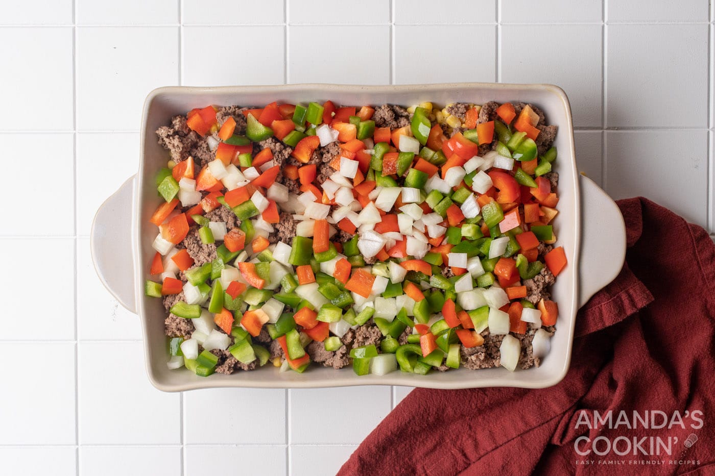 chopped peppers and onion on top of ground beef in a baking dish