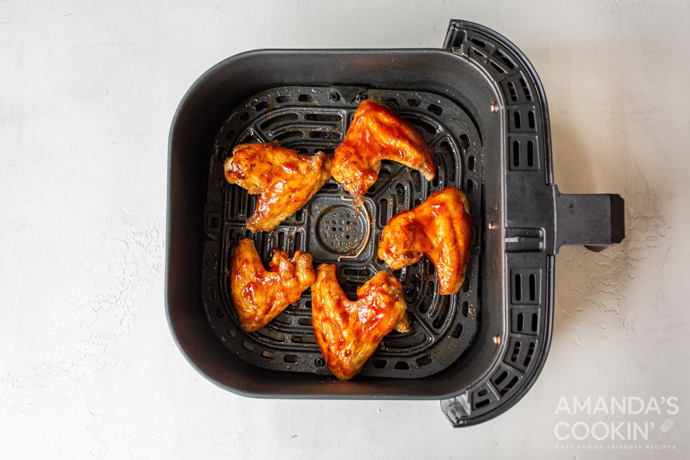 chicken wings in air fryer basket with sauce