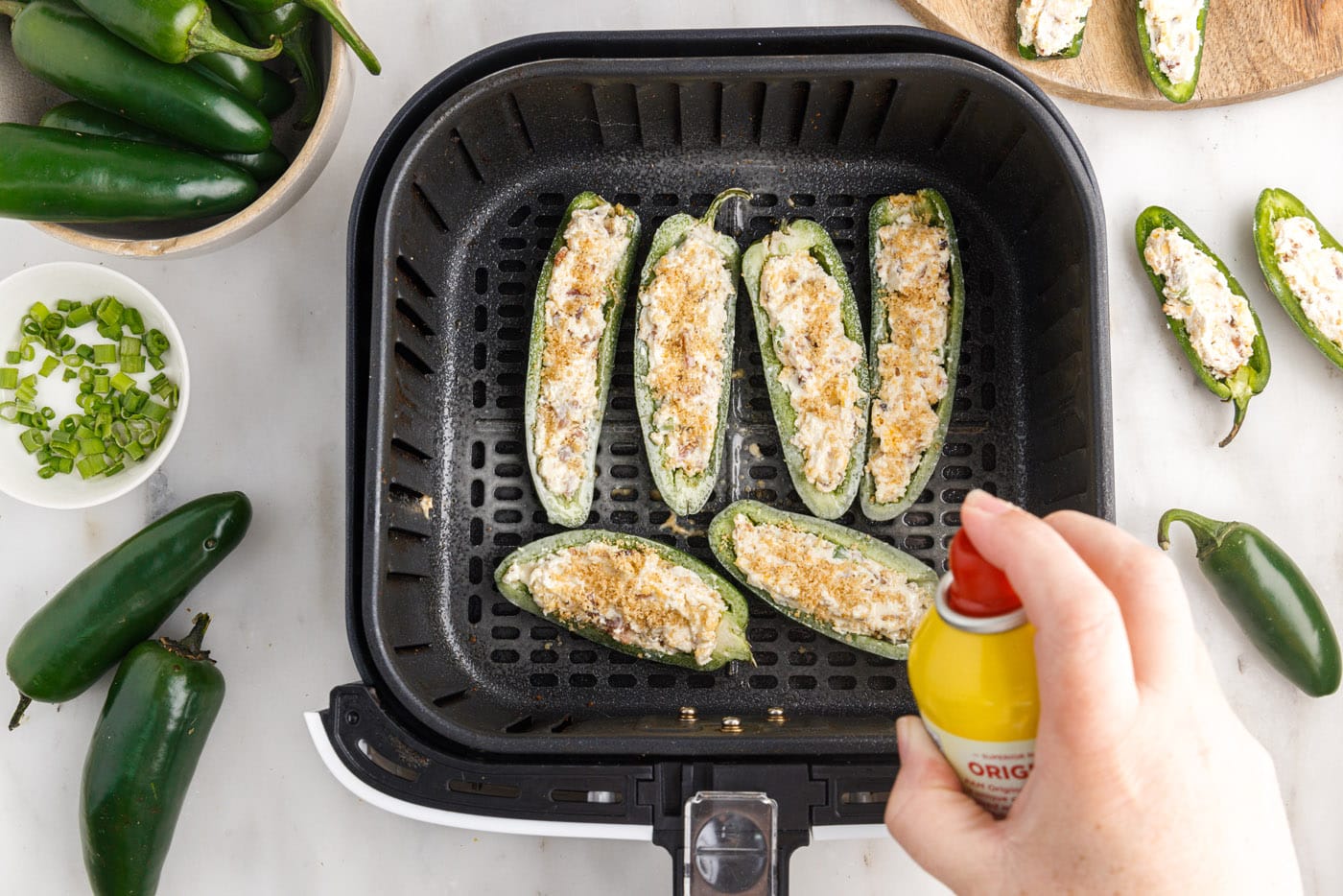 spraying non stick spray on jalapeno poppers in the air fryer basket