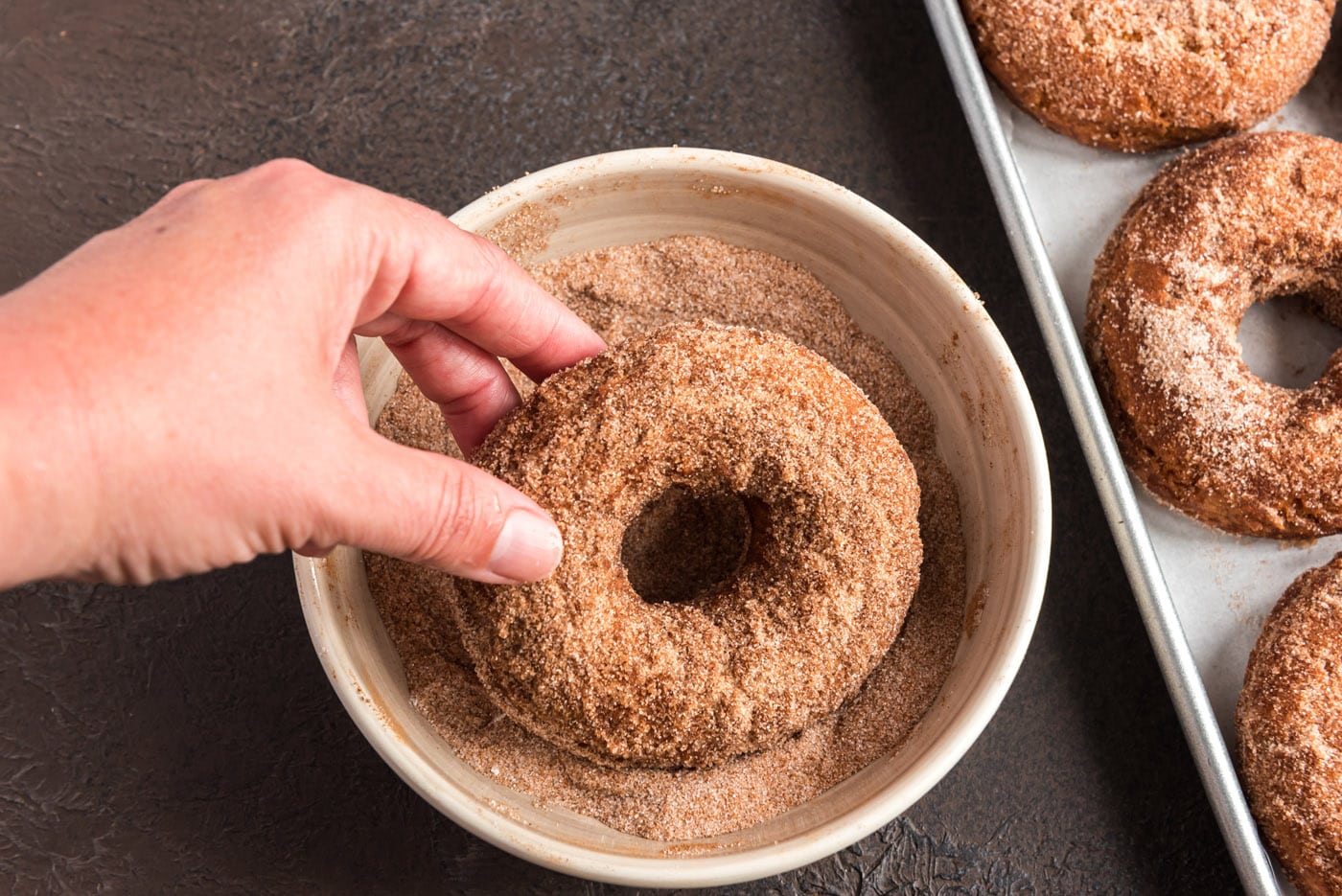 dipping fried donut in cinnamon sugar