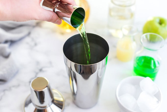 pouring apple vodka into a cocktail shaker