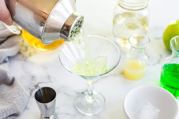 pouring shaken appletini into martini glass