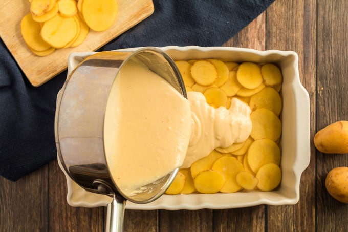 pouring cheese sauce over potatoes
