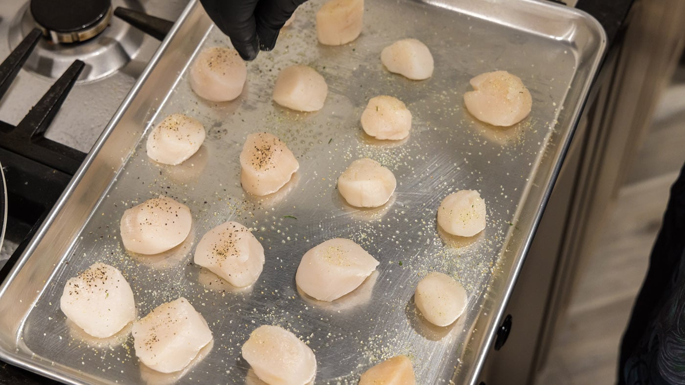 hand sprinkling garlic salt and pepper on scallops