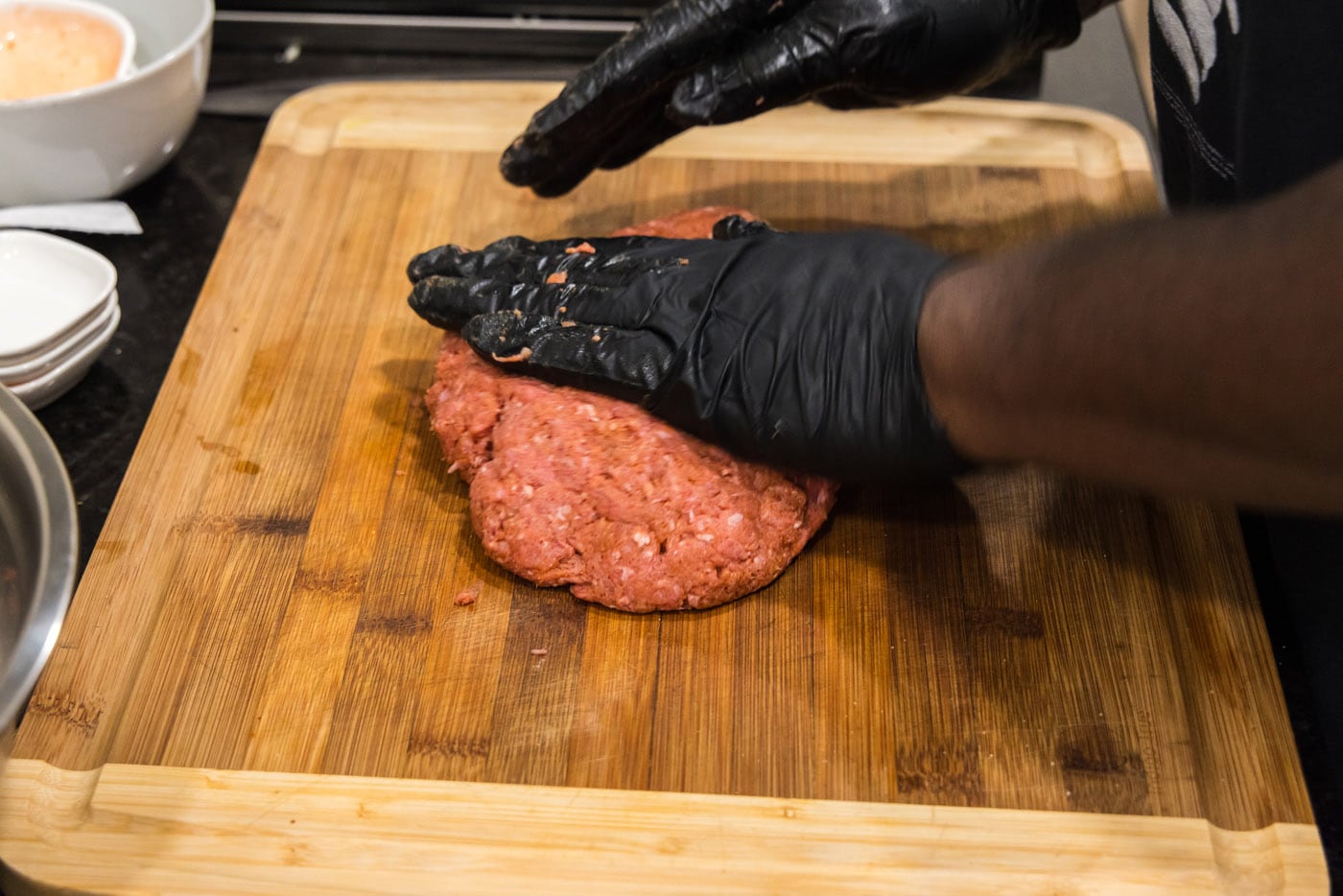 hands flattening burger meat on a cutting board