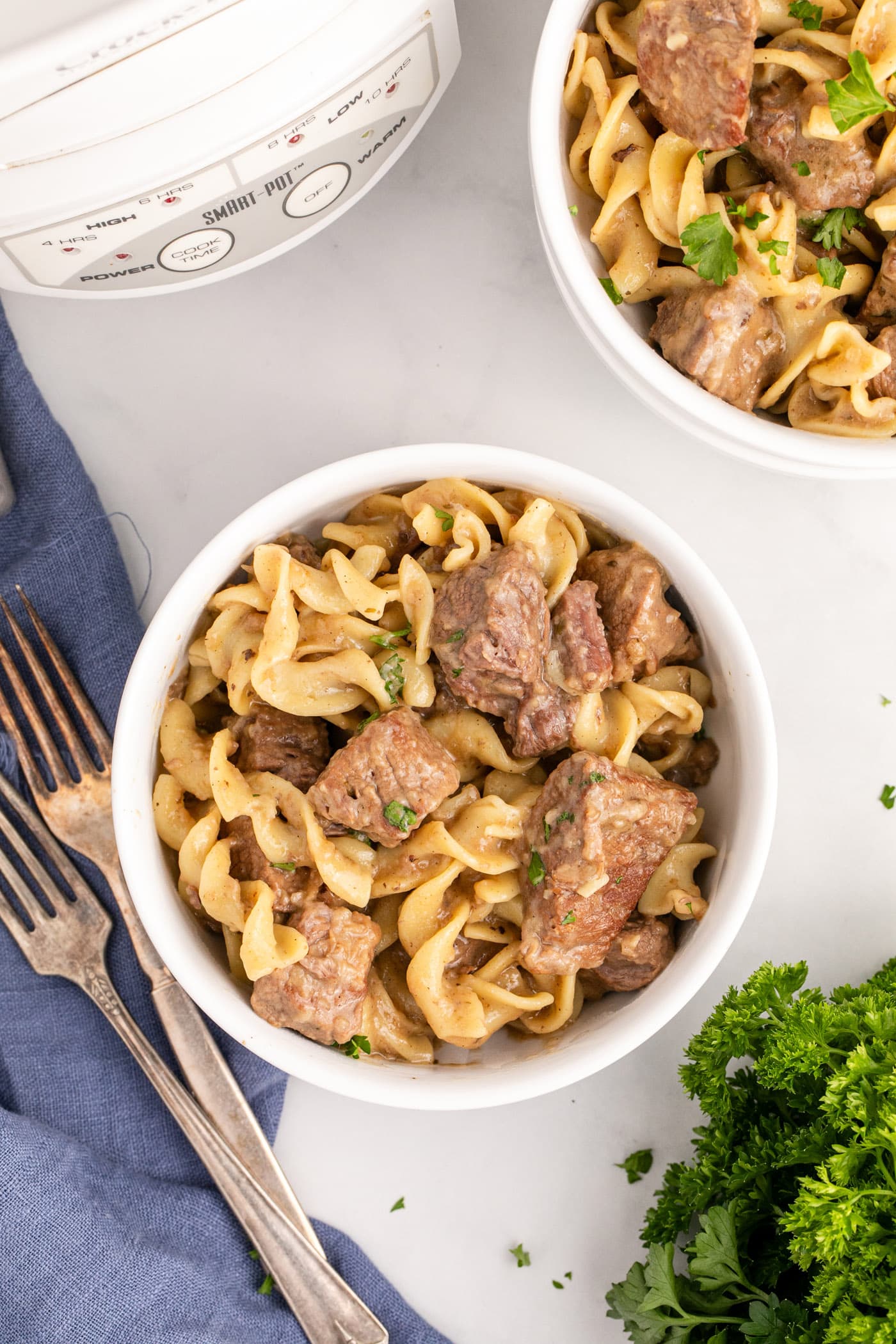 Two bowls of Beef and Noodles with a crockpot in the background