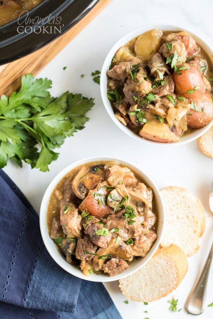 two bowls of beef stew on a white cutting board