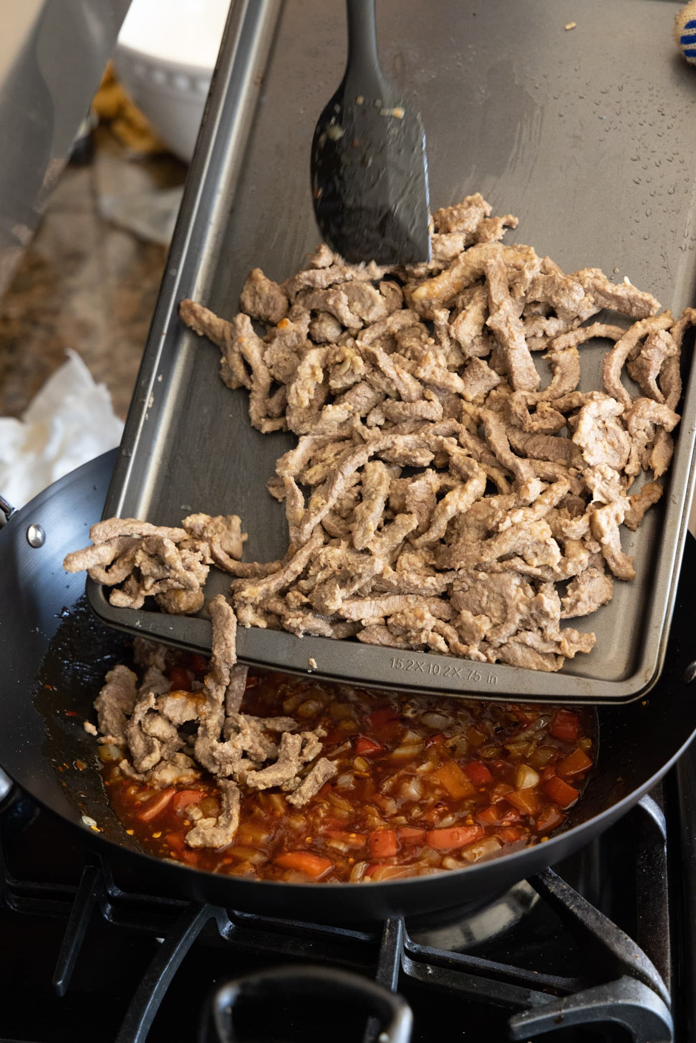 adding cooked beef to skillet with sauce and vegetables