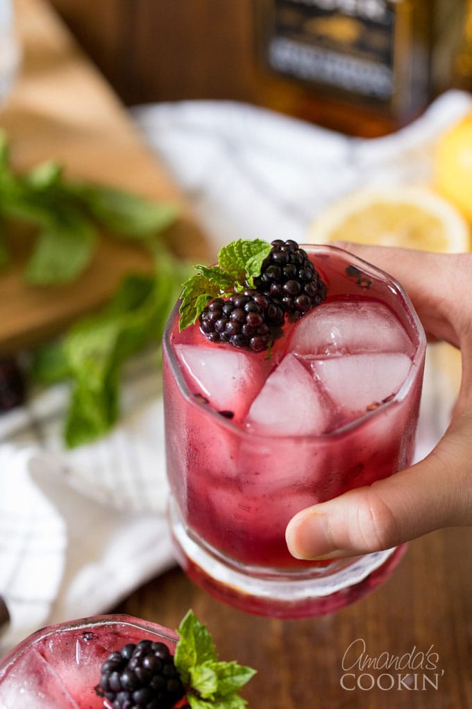 hand holding a glass of blackberry lemonade with whiskey