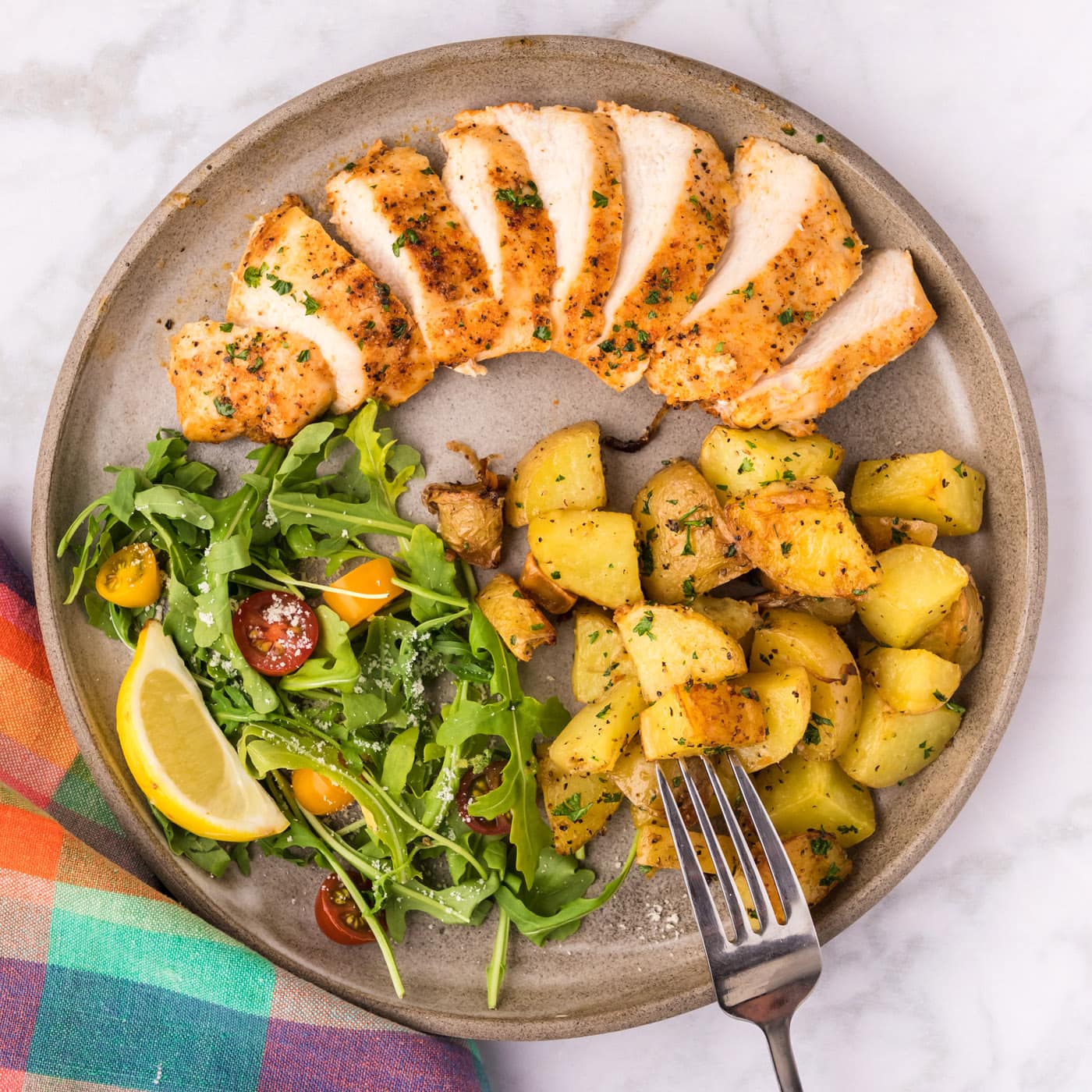 Overhead photo of Blackened Chicken on a plate with a salad, potatoes and a fork on the side