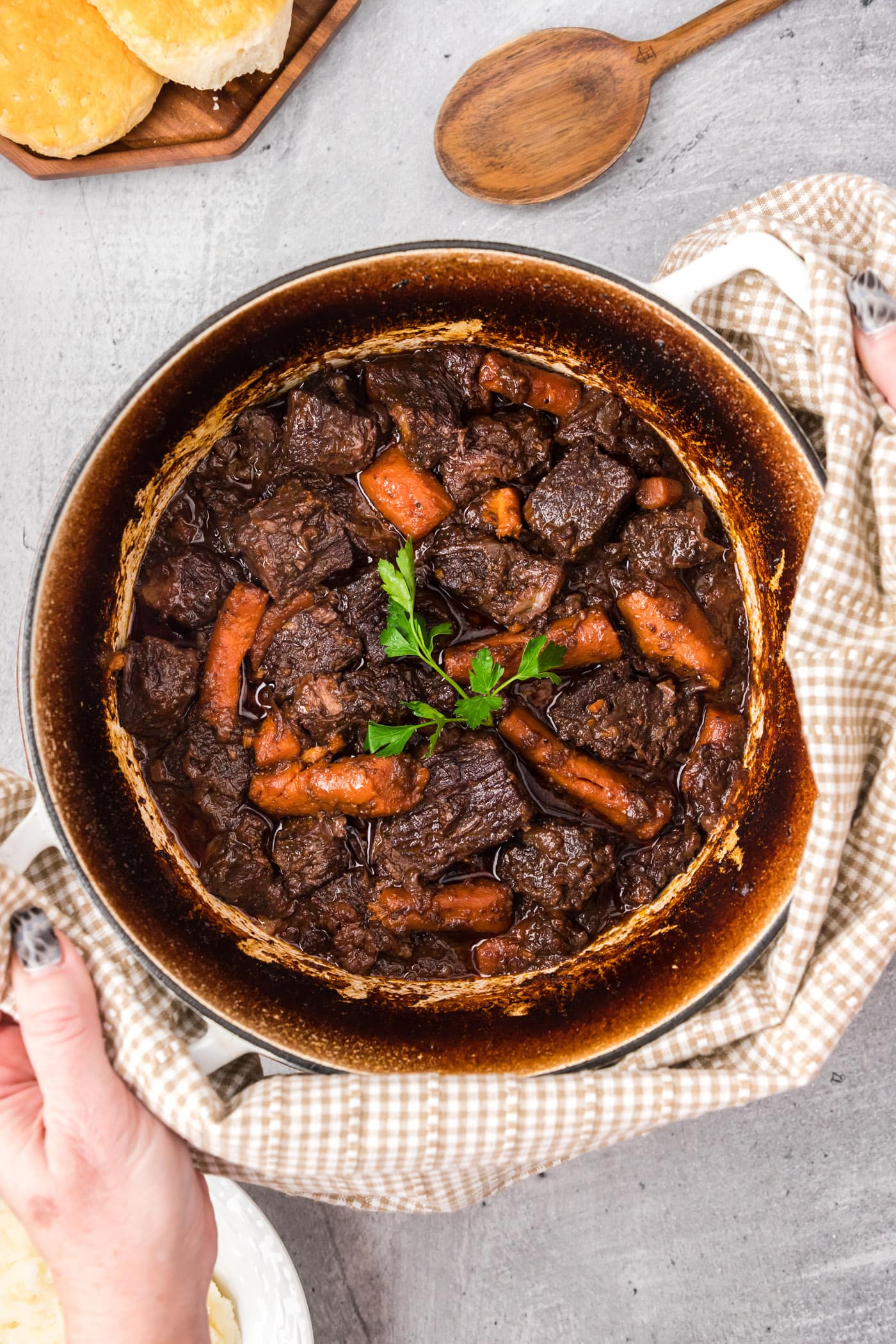 Hands holding a hot pot of Braised Beef with a towel