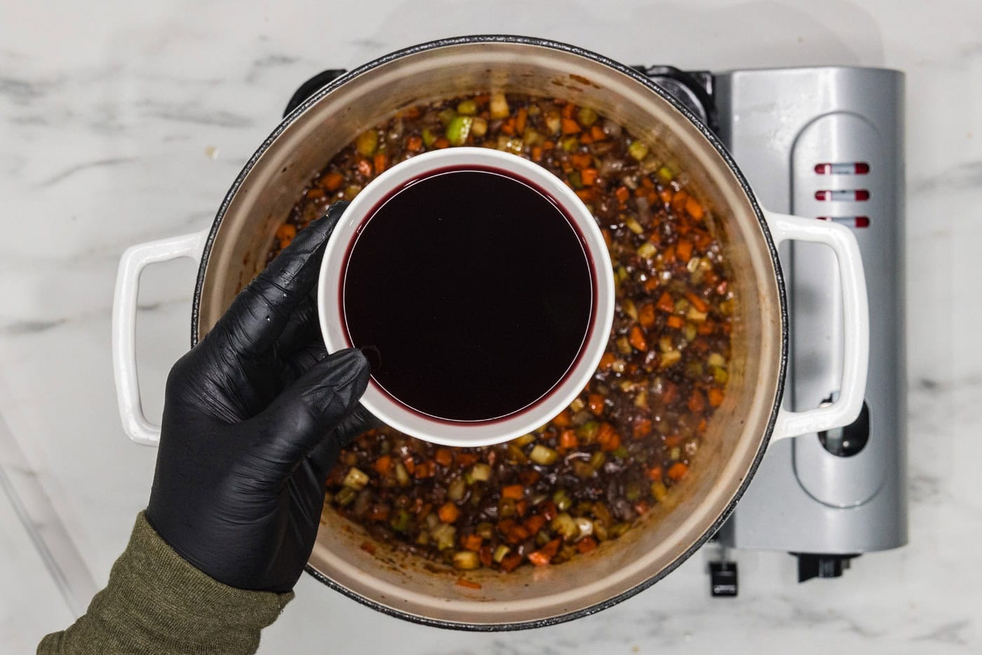 Red wine in a bowl over a dutch oven of vegetables