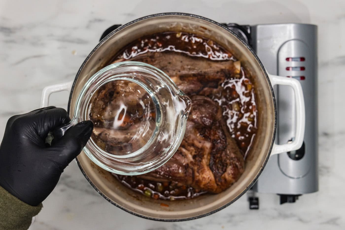 pouring water into dutch oven with braised lamb shanks