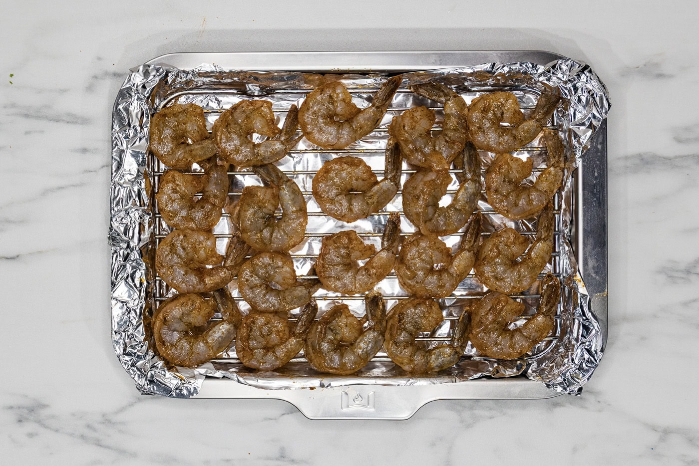 seasoned shrimp on a foil lined baking sheet with a wire rack