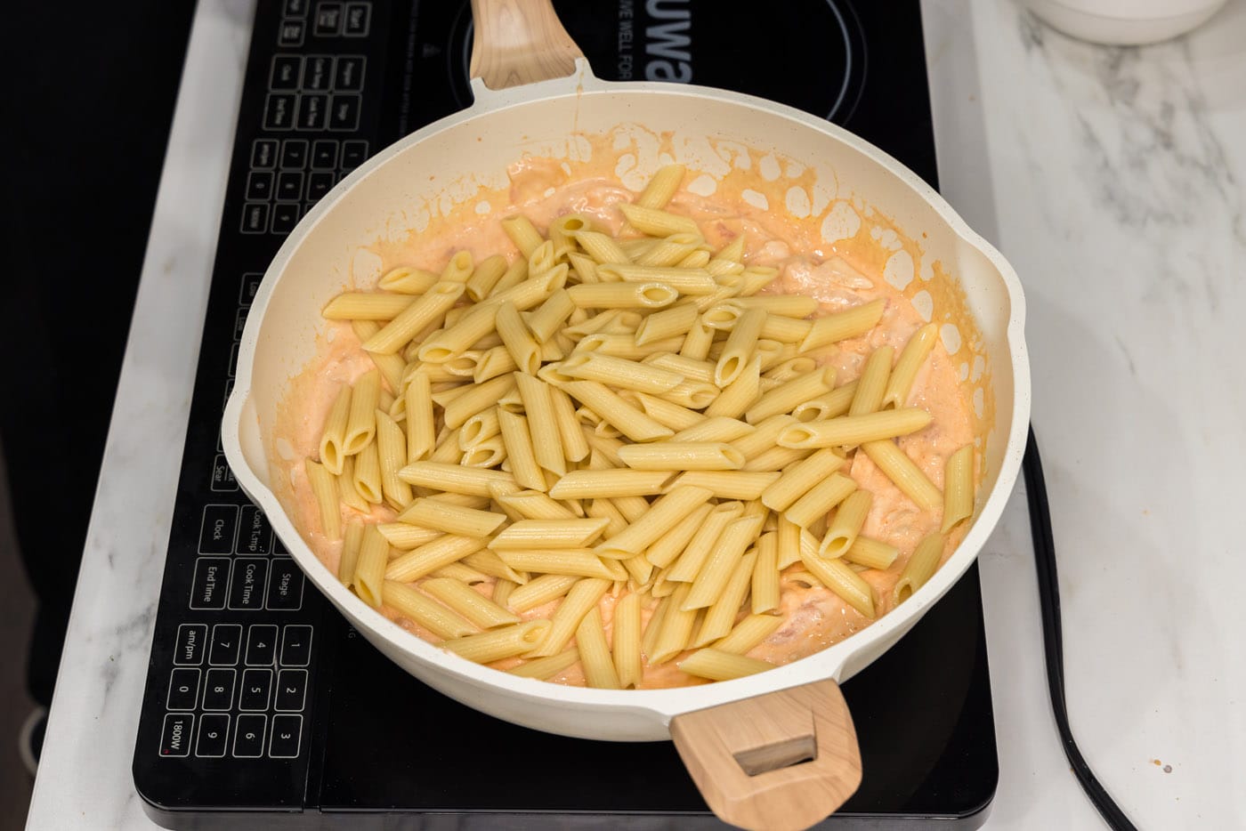 adding pasta to skillet with creamy buffalo sauce