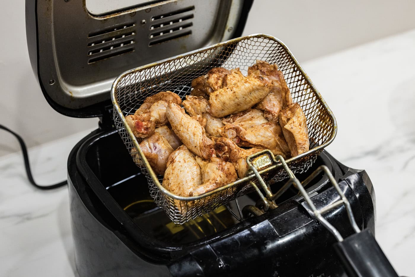 lowering basket of chicken wings into a deep fryer with oil