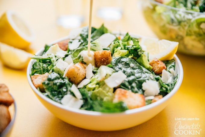 dressing being added to a bowl of salad