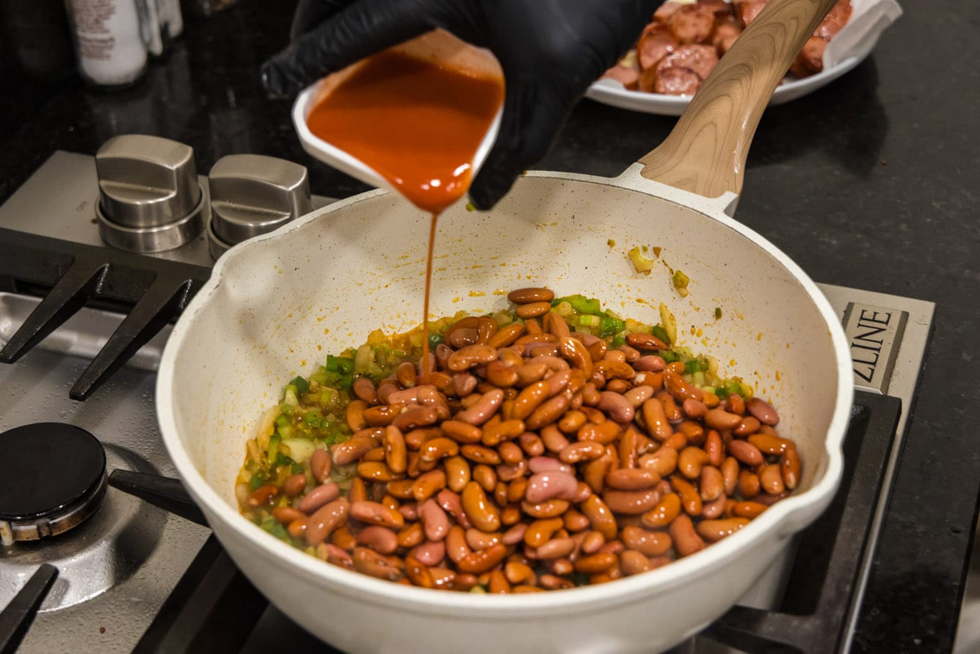 pouring hot sauce into skillet with red beans and vegetables