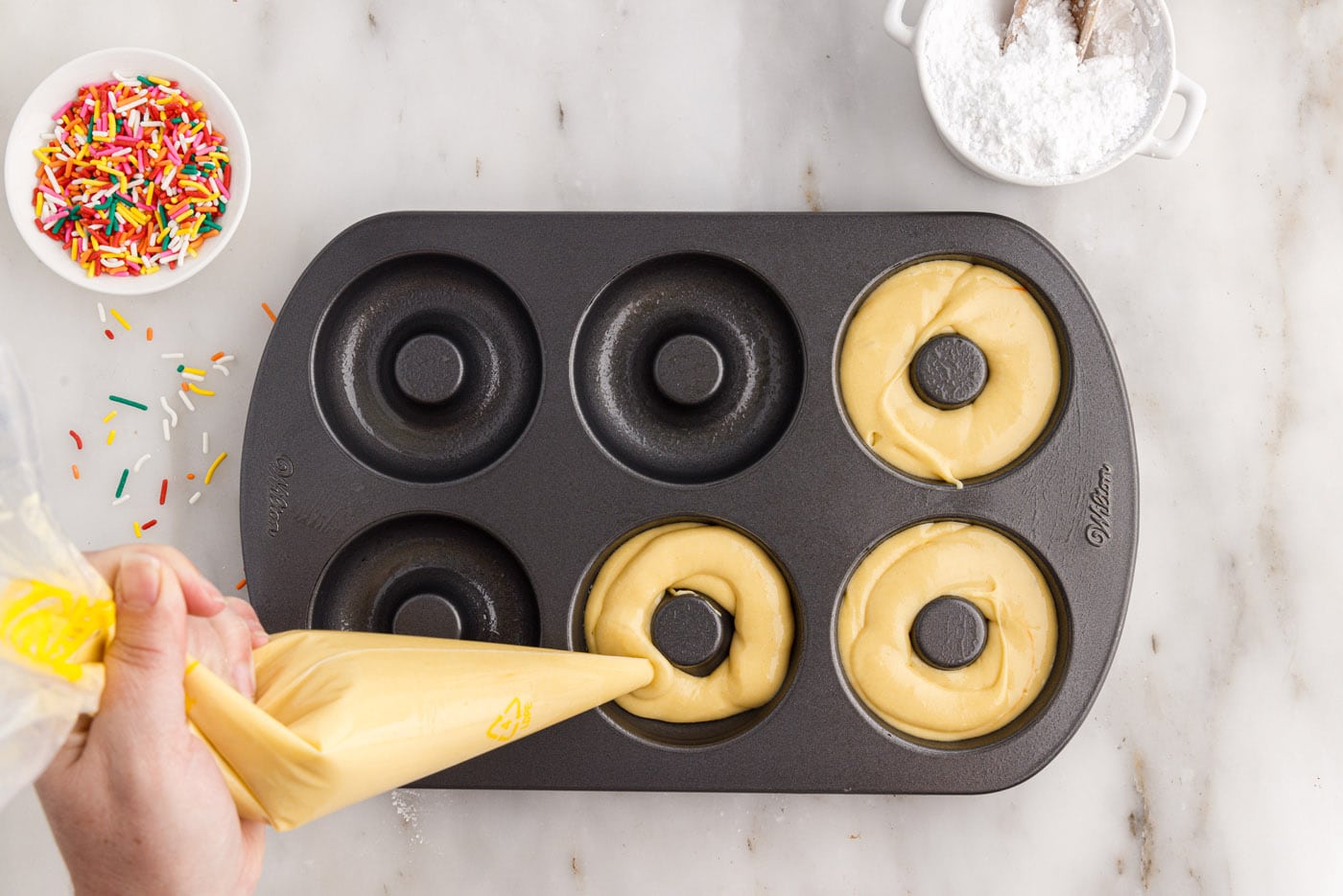 piping cake mix donut batter into a donut pan