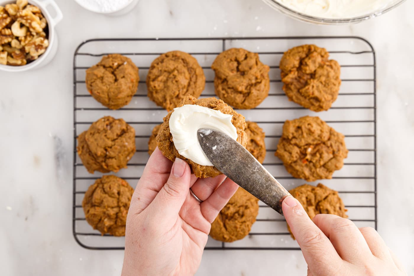 spatula smearing frosting onto carrot cake cookies
