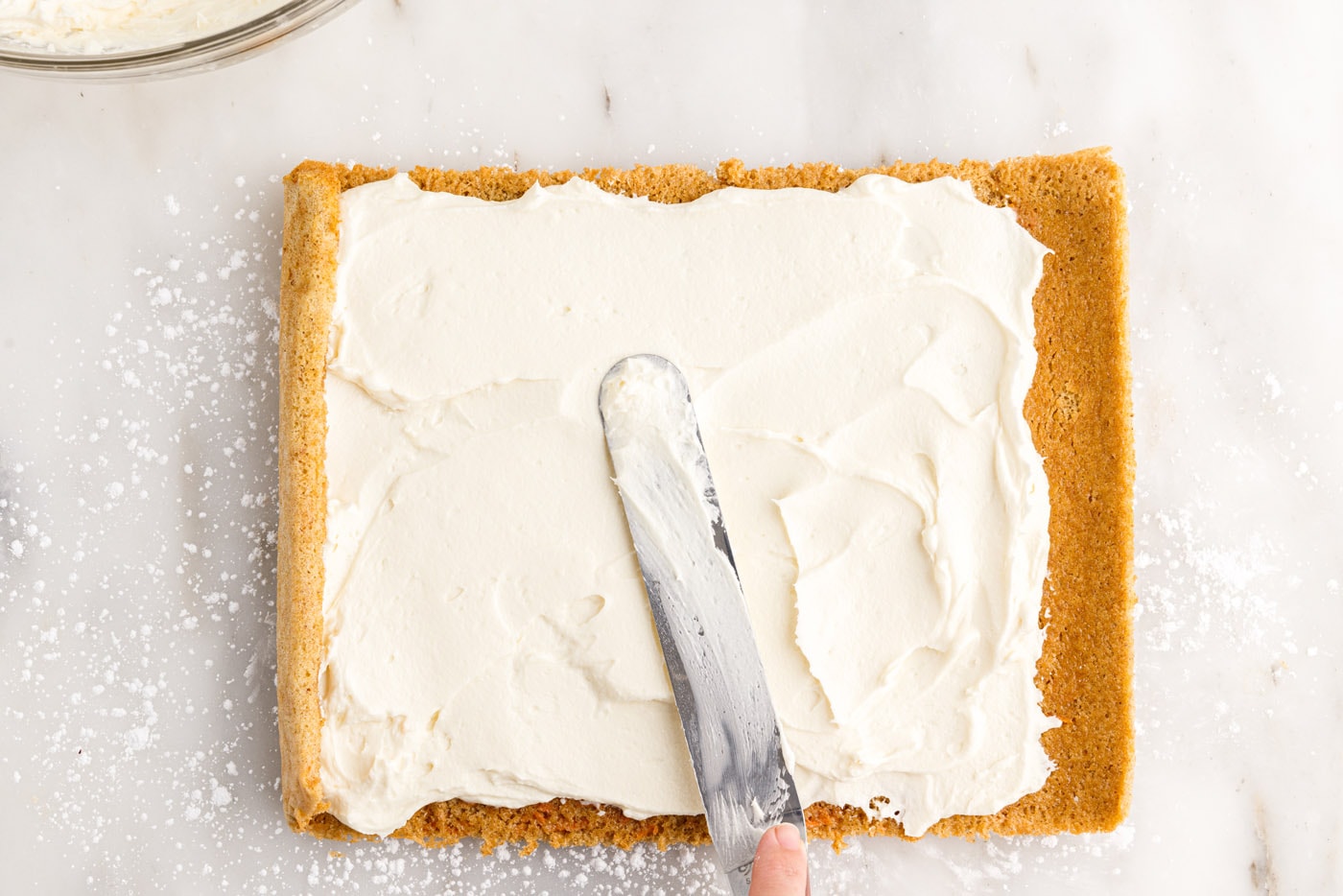 spreading cream cheese filling on top of carrot cake