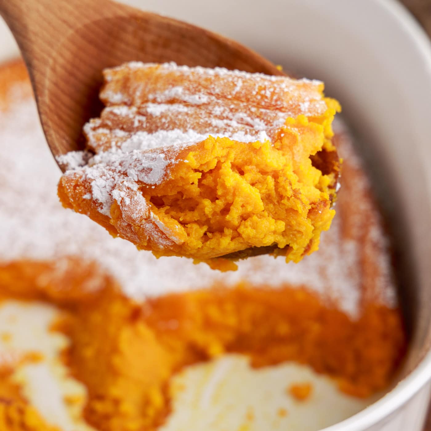 Spoonful of Carrot Souffle held above a dish of Carrot Souffle