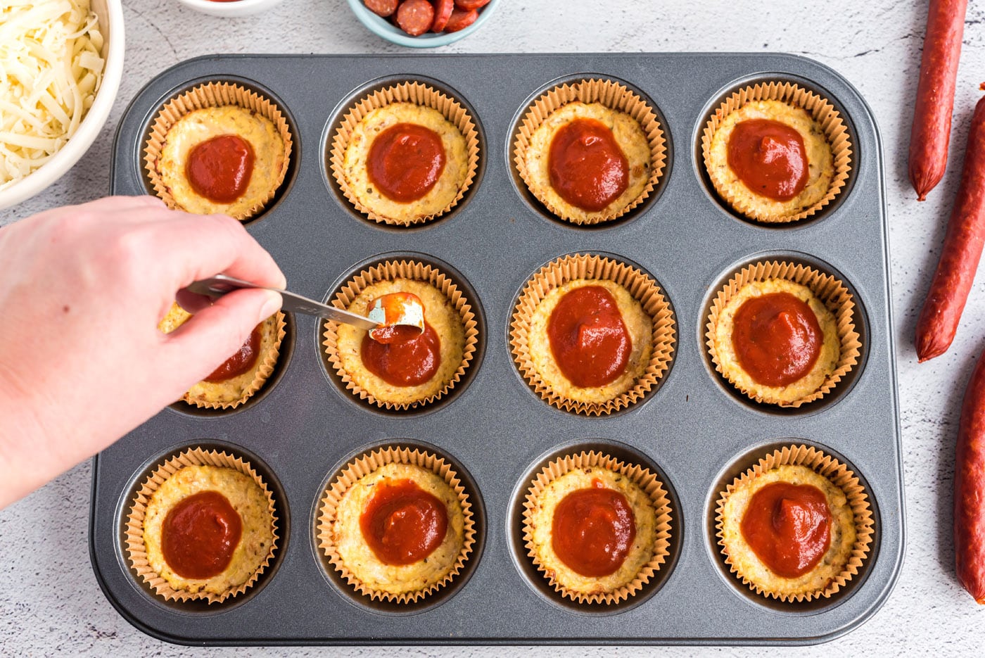 spooning pizza sauce on top of cauliflower pizza bites