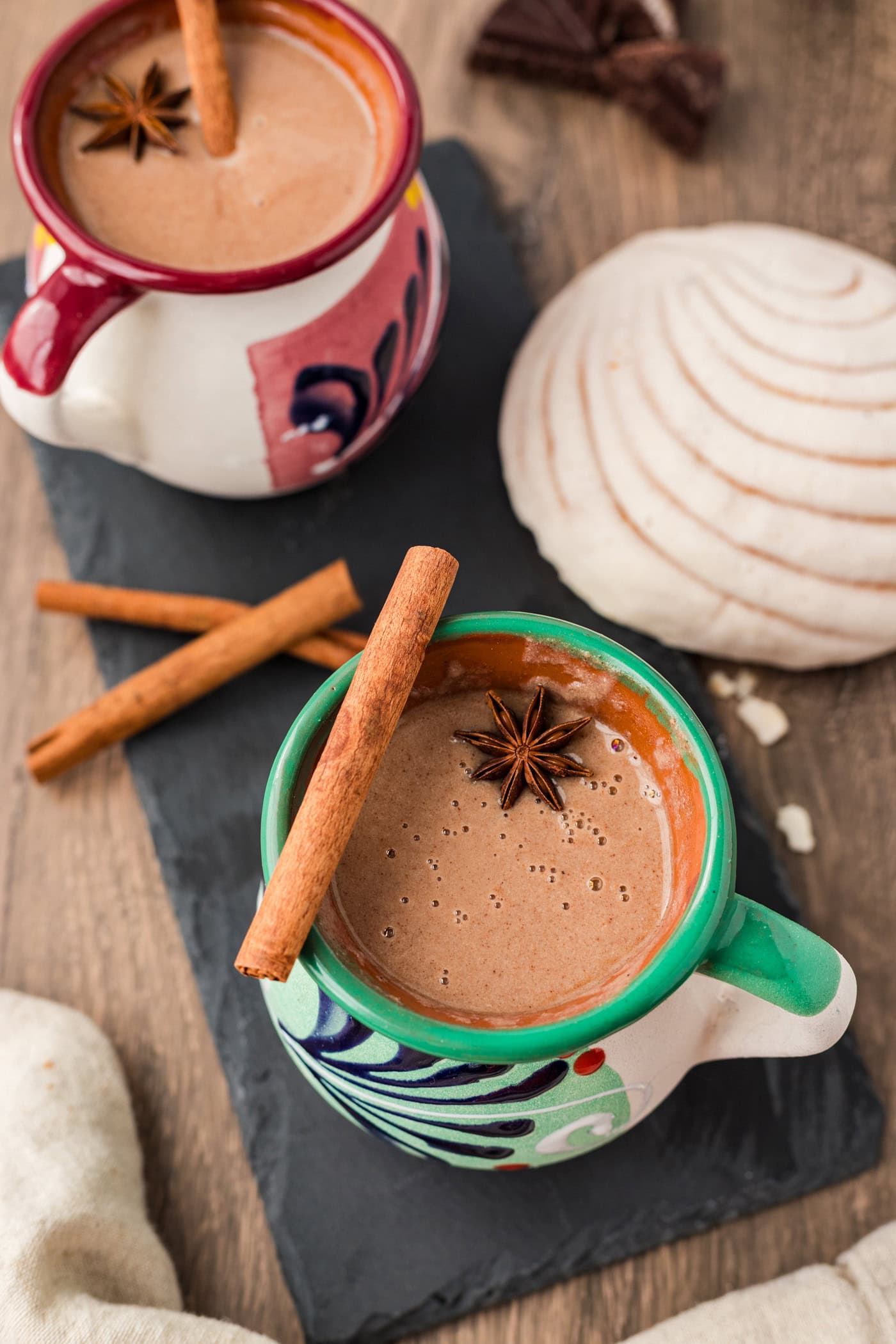 Two mugs of Champurrado with a cinnamon stick and star anise resting on top