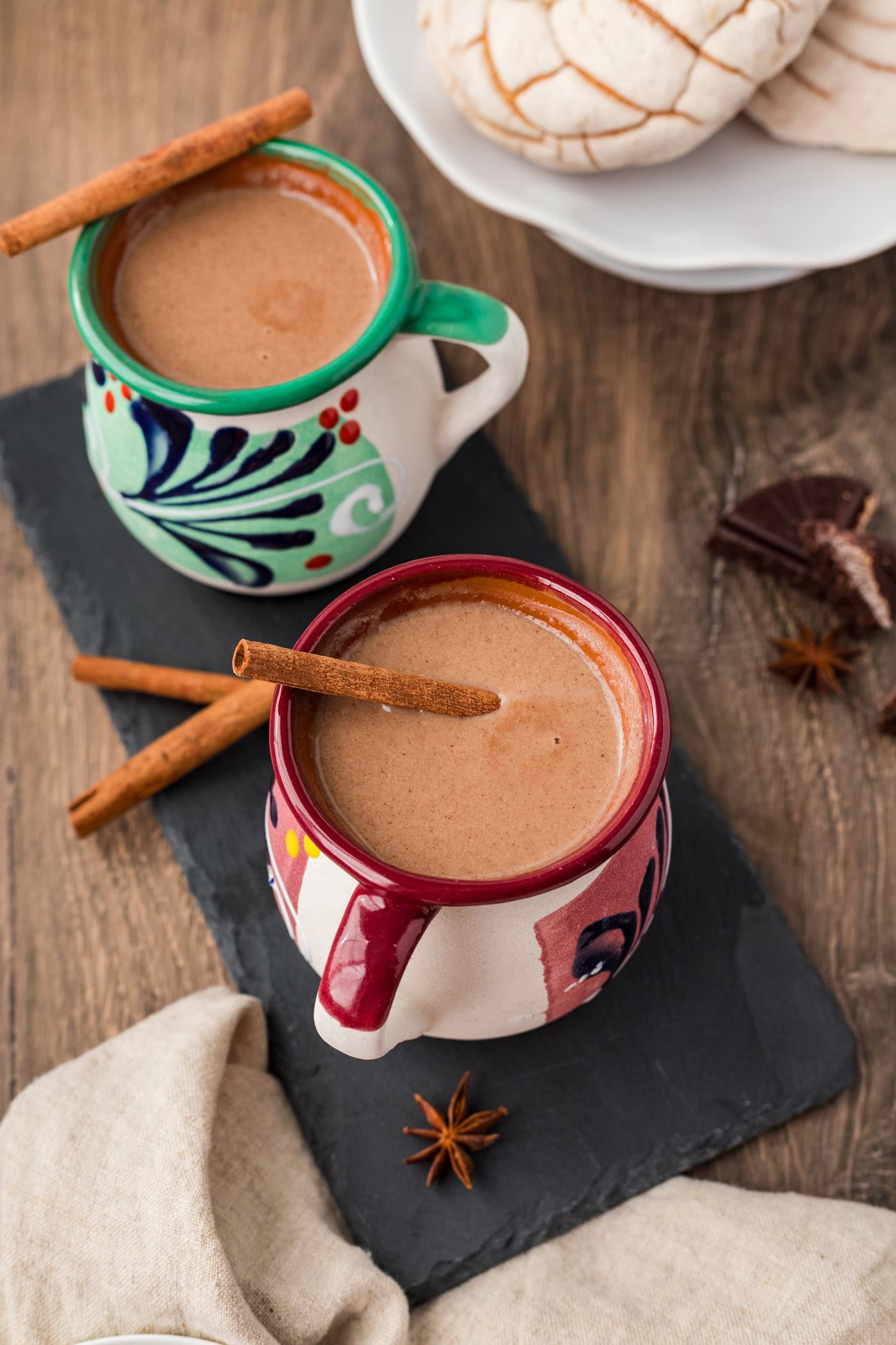 Two mugs of Champurrado with a cinnamon stick resting on top