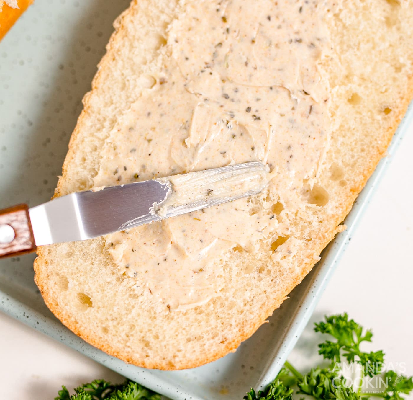 butter knife smearing seasoned butter onto french bread
