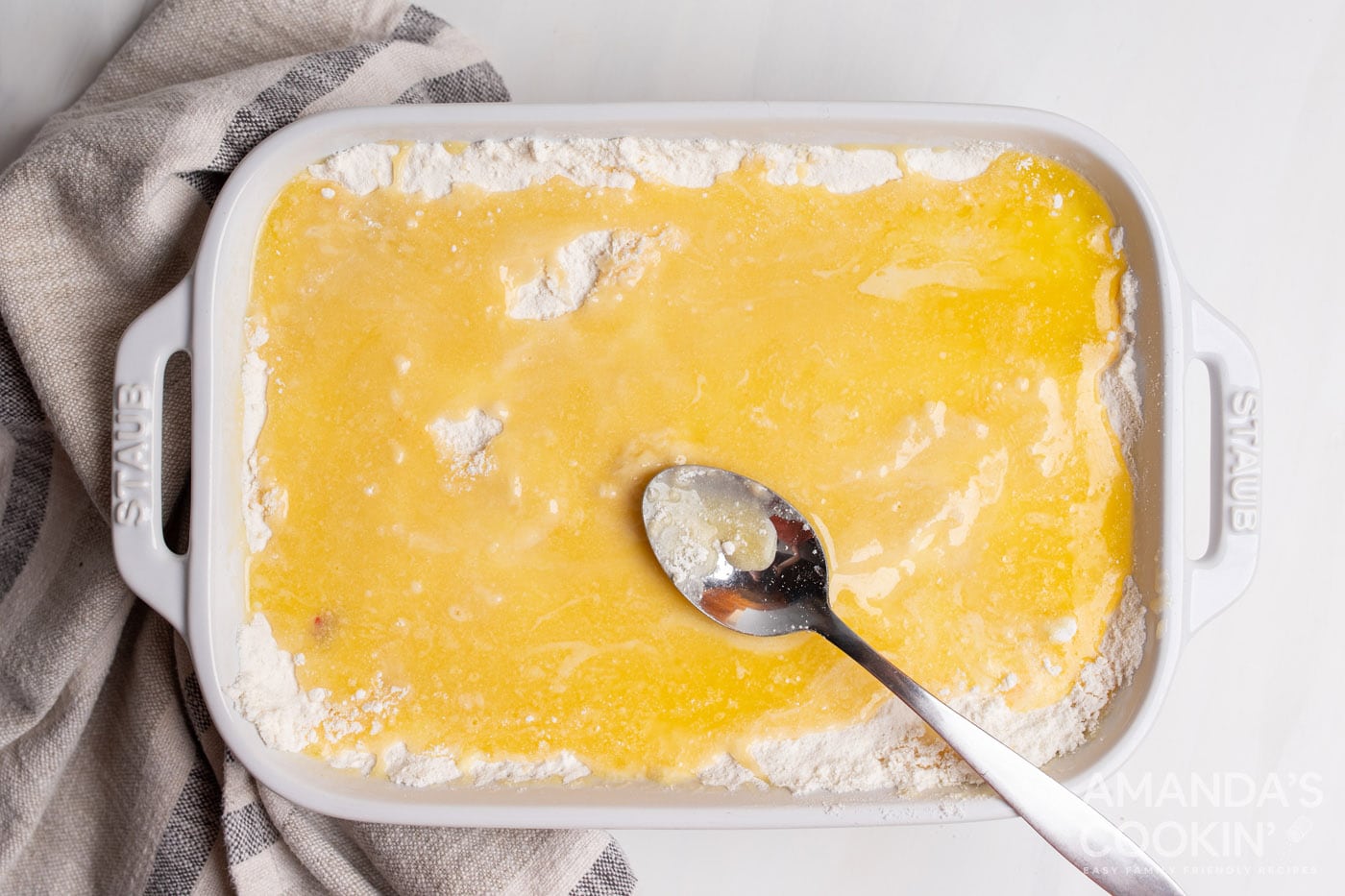 spooning butter over cake mix in a casserole dish