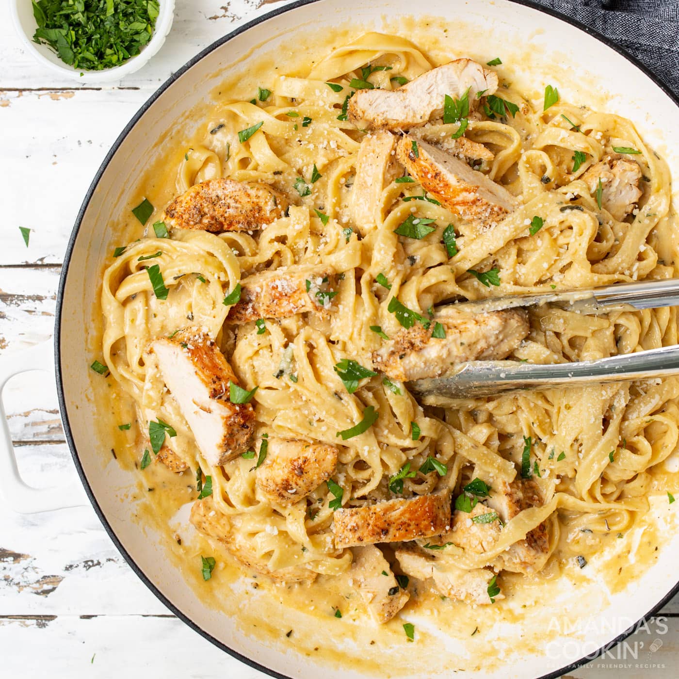 Chicken Alfredo in a serving dish with tongs