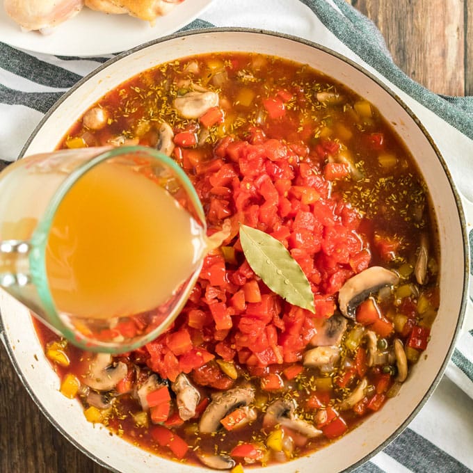 tomatoes, broth, and bay leaf over ingredients in skillet