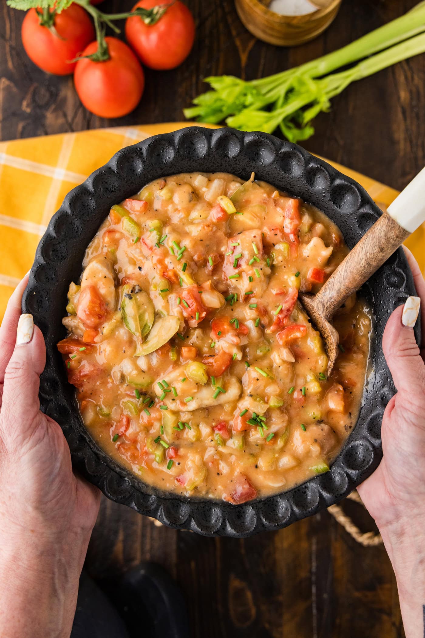 Hands holding up a bowl of Chicken Etouffee with a spoon in it