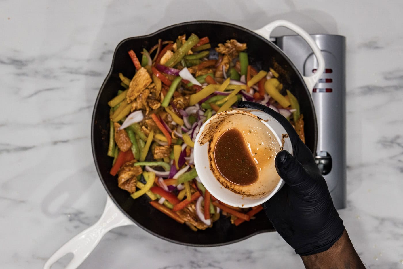 pouring remaining marinade into skillet with chicken fajitas