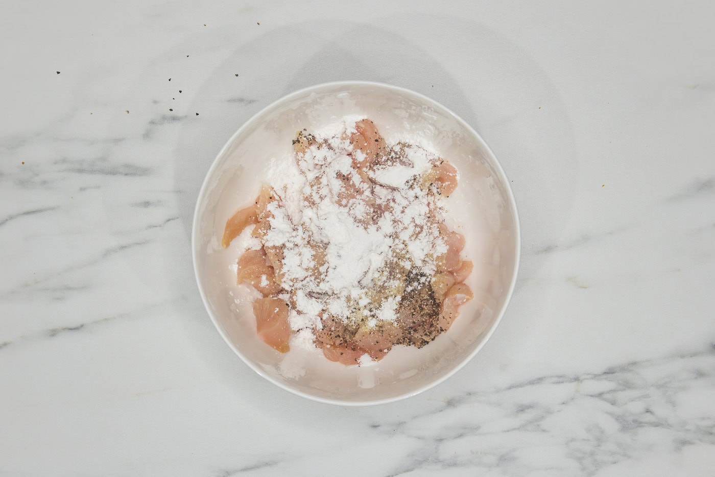 raw chicken pieces in a bowl with cornstarch and seasonings