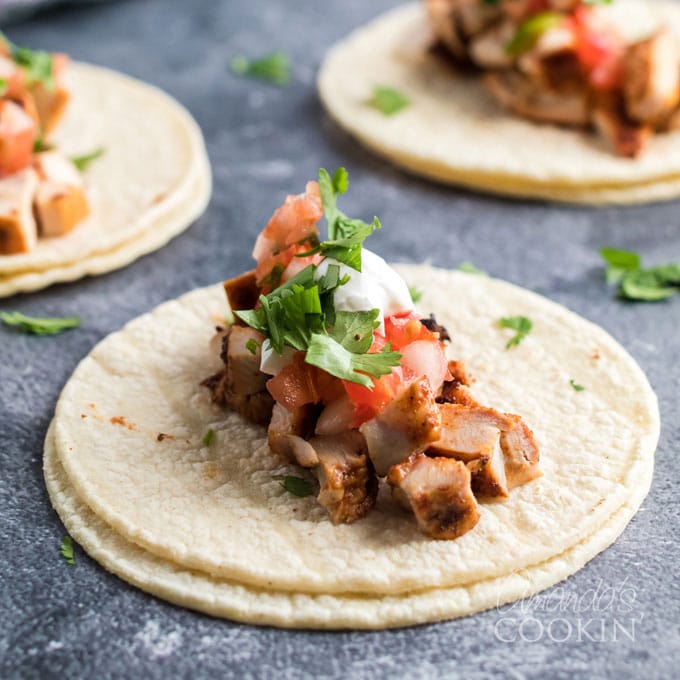 two corn tortillas with chicken taco filling and toppings