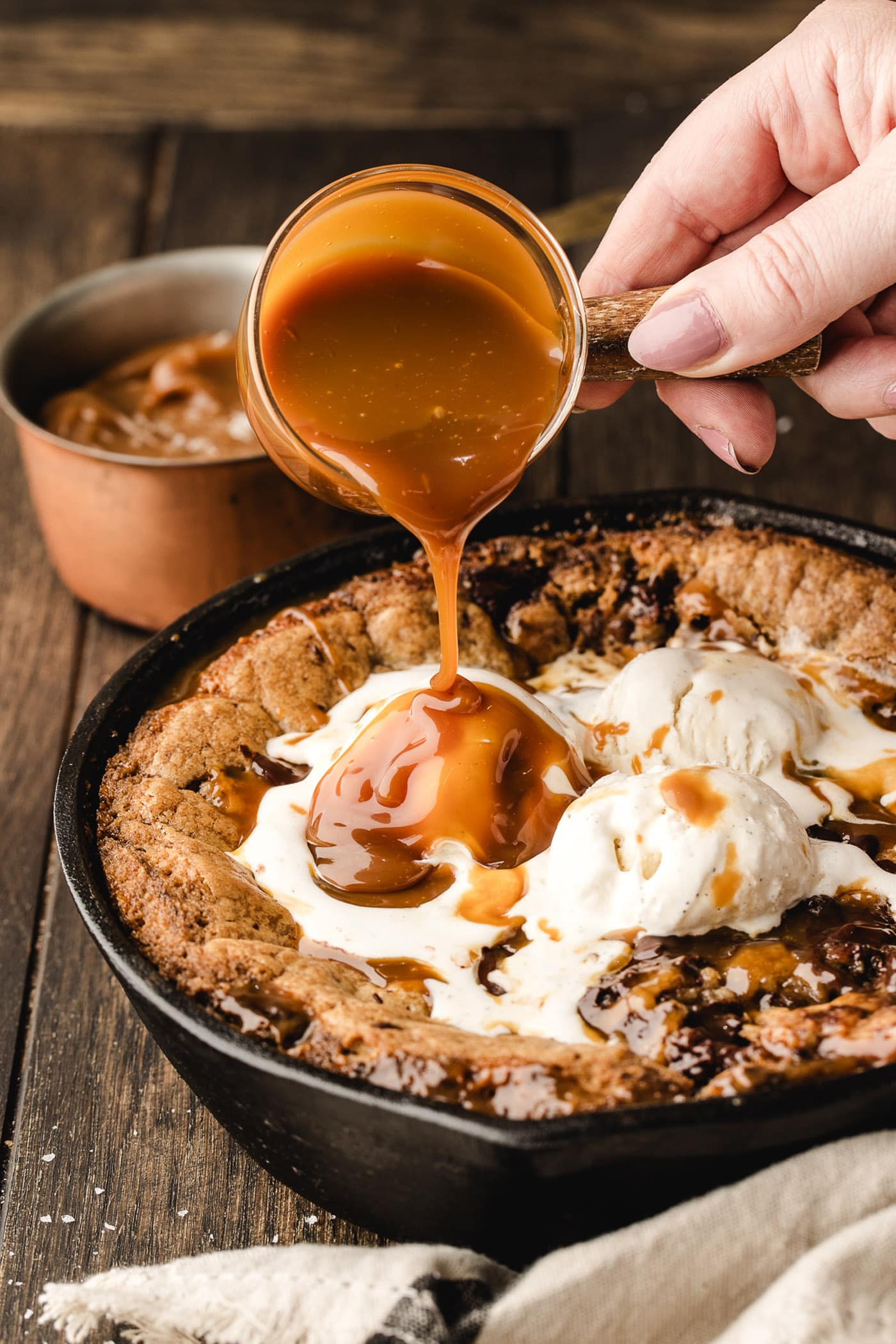 Caramel sauce being poured on top of a Chocolate Chip Caramel Skillet Cookie