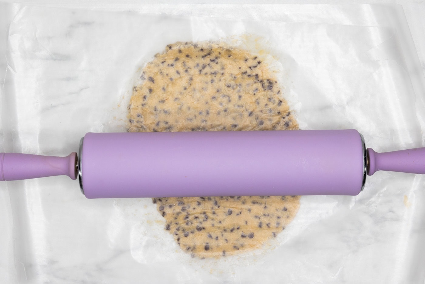 rolling pin flattening cookie dough ball between parchment paper