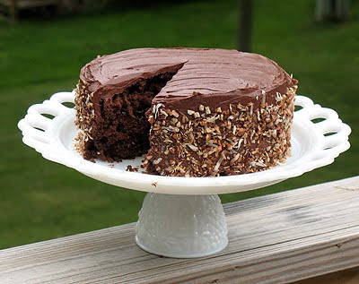 A photo of a chocolate sauerkraut cake with a slice missing on a white cake stand.
