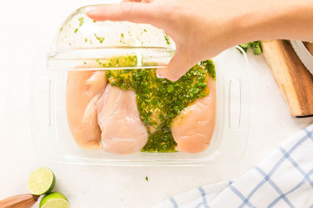 woman pouring marinade over chicken in a glass dish
