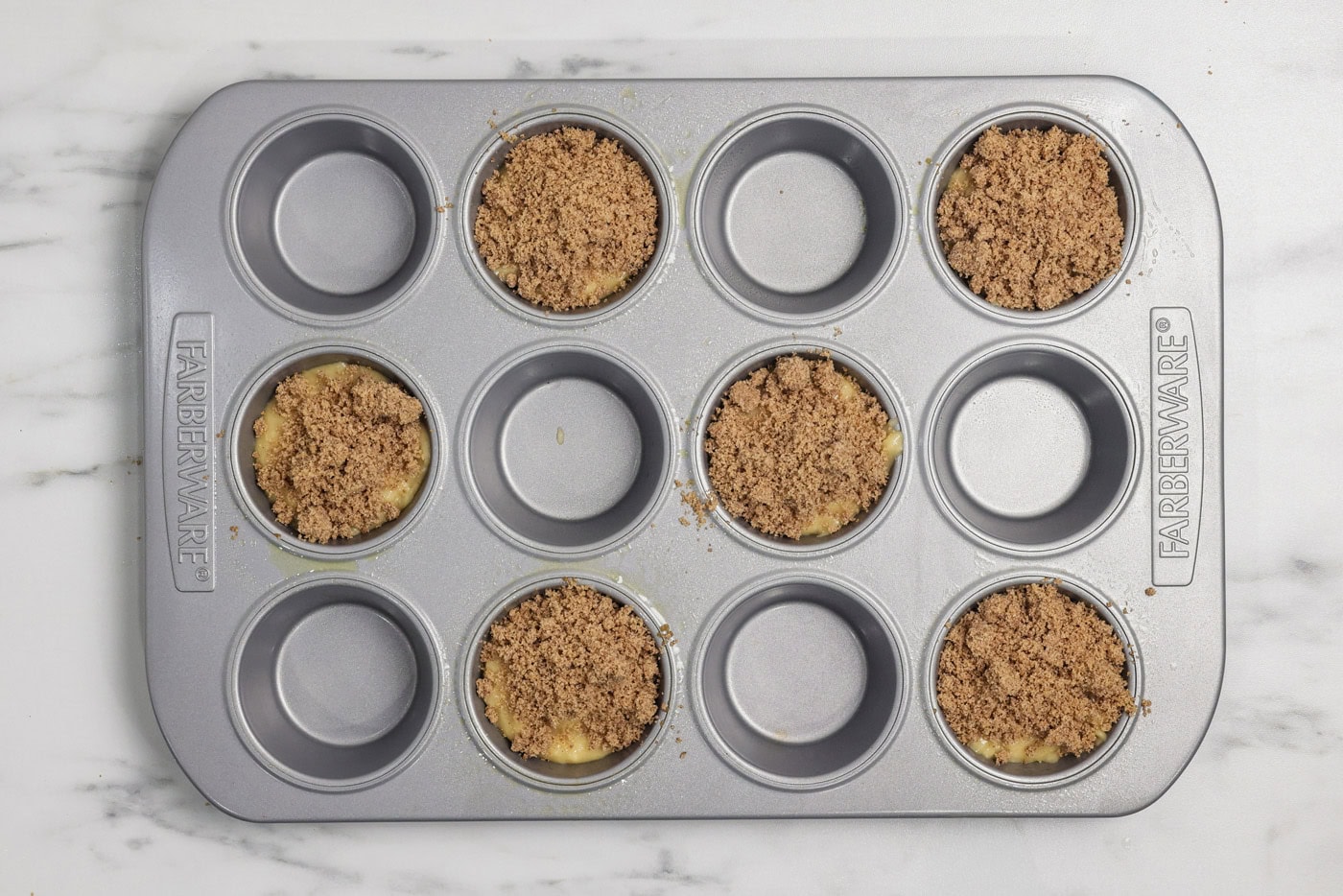 Cinnamon streusel added on top of vanilla muffin batter in a muffin pan