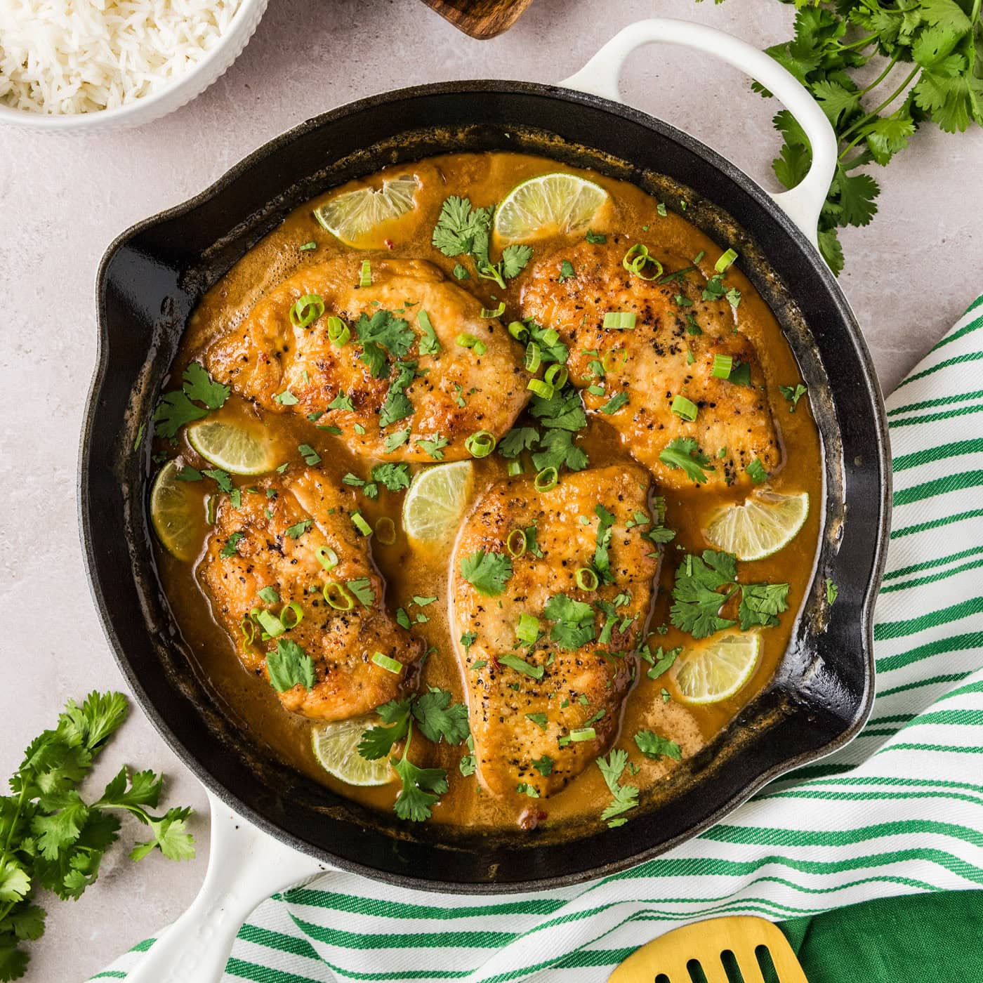 Coconut Chicken in a skillet with rice, herbs and linens on the side