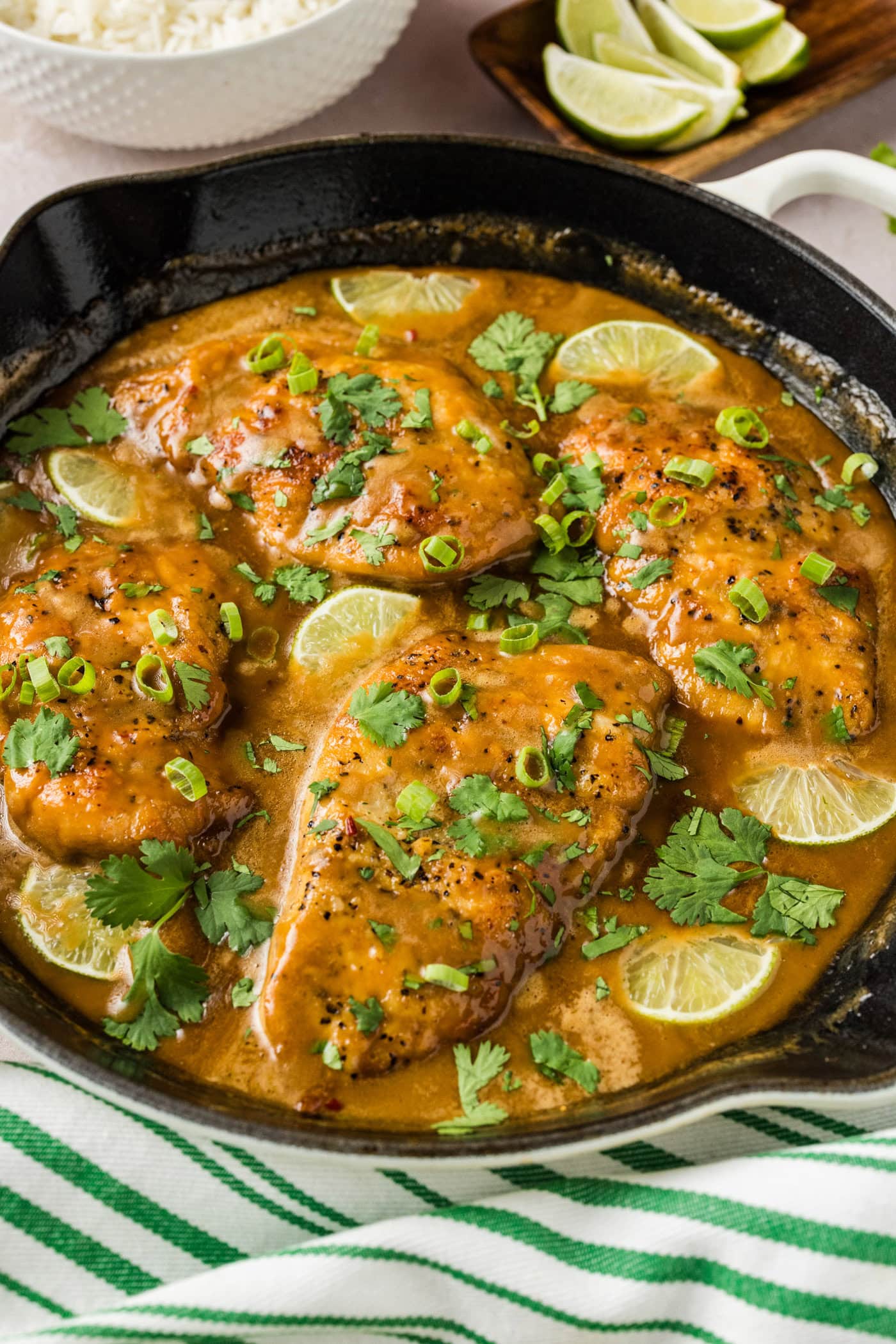 Coconut Chicken in a skillet with rice and limes in the background