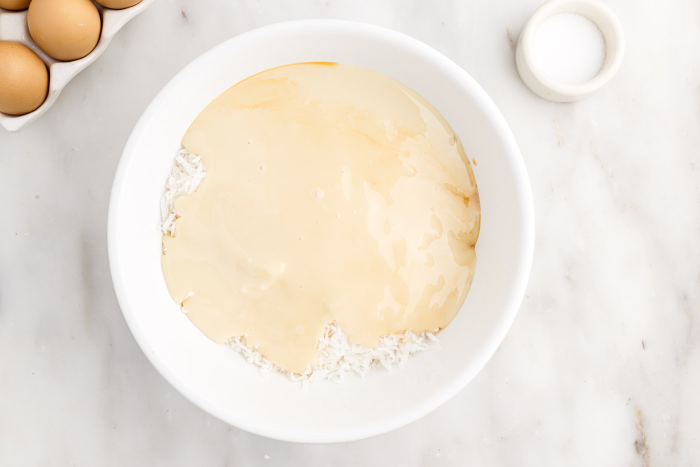 sweetened condensed milk with shredded coconut and vanilla in a bowl