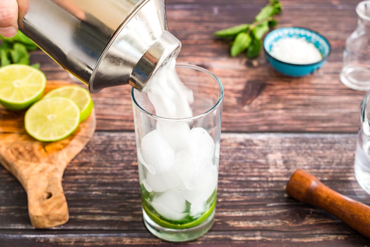 straining coconut mojito into a glass