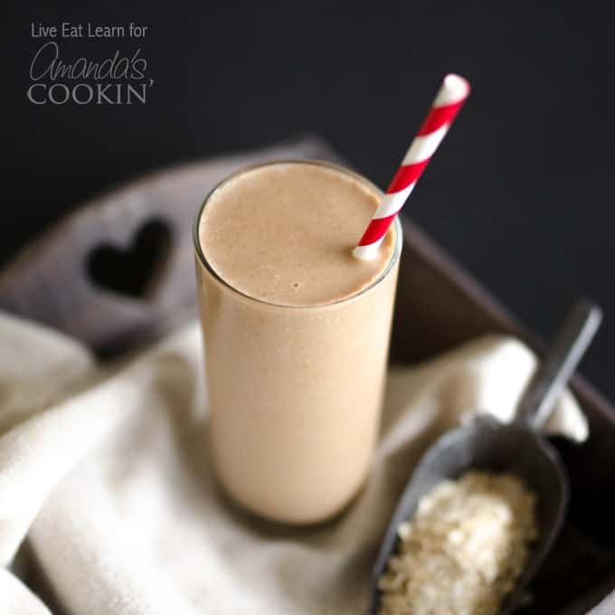 A close up photo of a tall loaded coffee breakfast smoothie served with a red and white straw.