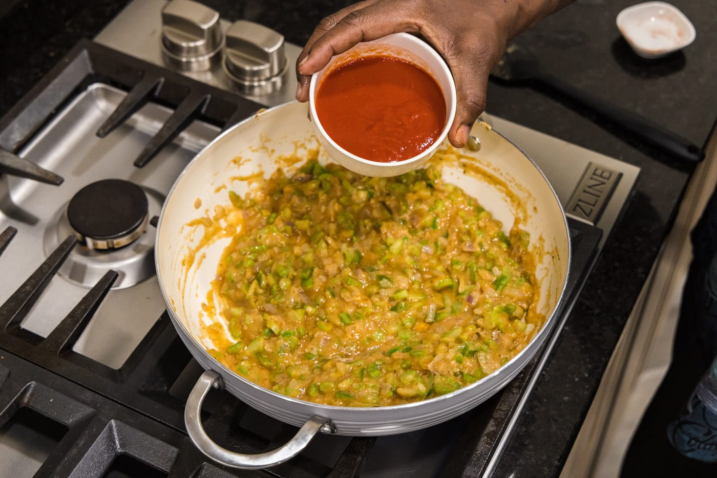 pouring tomato sauce into skillet with vegetable roux