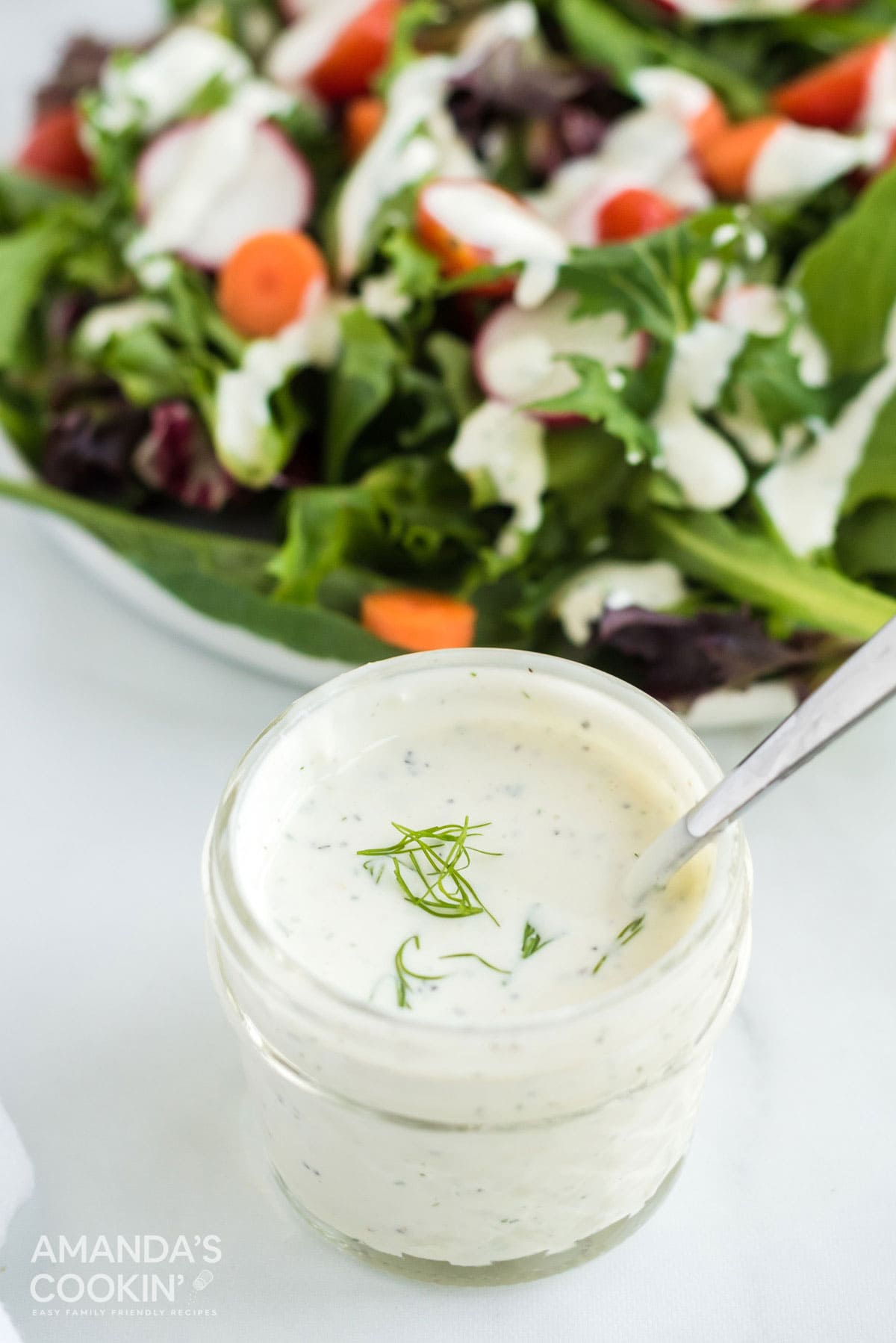 jelly jar of dill dressing with salad behind it
