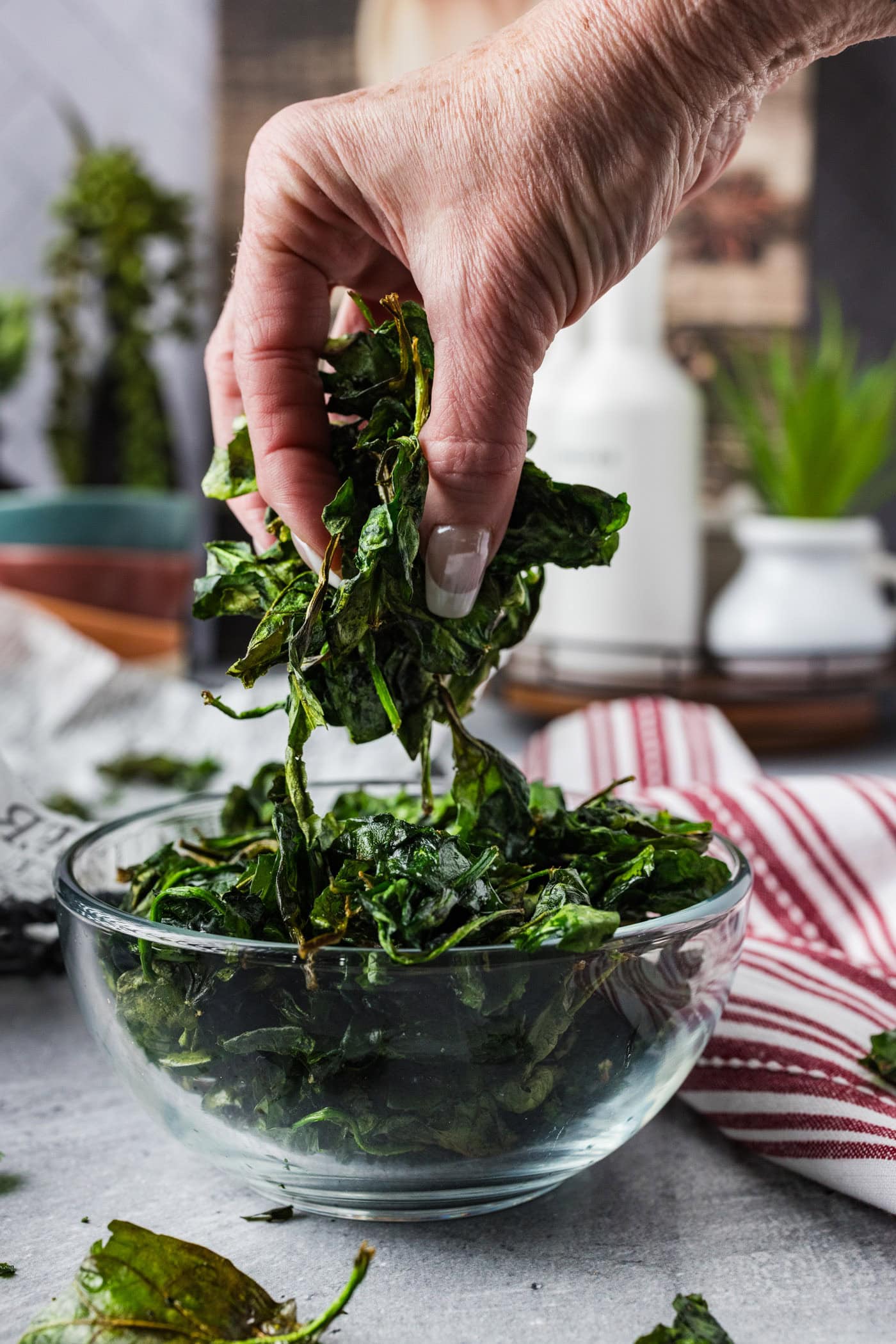 Handful of Crispy Air Fryer Spinach held above a bowl of Crispy Air Fryer Spinach